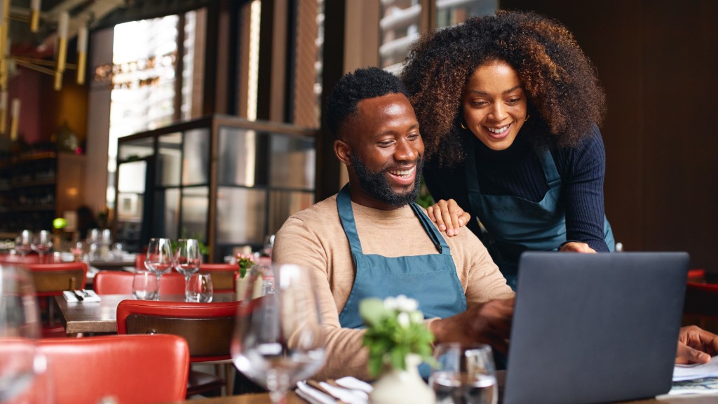 Two small business owners reviewing work on a laptop in a restaurant, representing AI support for small business operations and team efficiency.